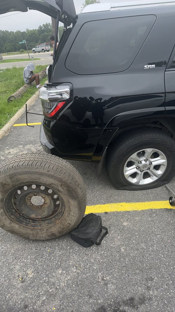 Flat tire assistance on an SUV pulled over on the roadside with the spare tire ready